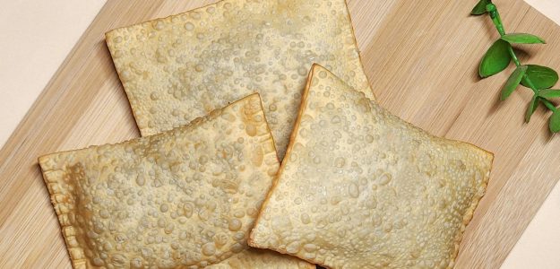 Golden brown fried pastries on a wooden chopping board with green leaves.