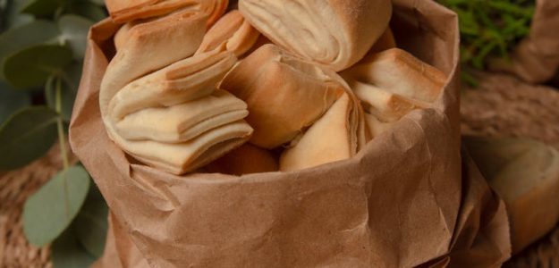 Freshly baked artisan bread in a rustic brown bag on a woven surface.